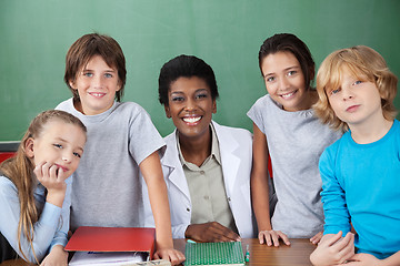 Image showing Cute Schoolchildren With Female Teacher At Desk