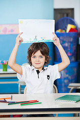 Image showing Boy Holding Drawing Paper At Desk In Kindergarten