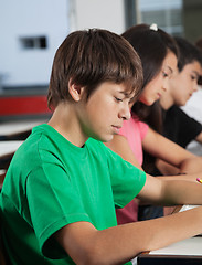 Image showing Schoolboy Studying At Desk With Classmates In Background