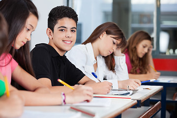 Image showing Teenage Boy Sitting With Friends Writing At Desk