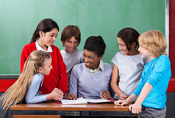 Image showing Happy Teacher Teaching Schoolchildren At Desk In Classroom