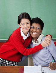 Image showing Schoolgirl Hugging Female Teacher At Desk