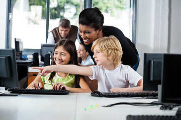 Image showing Teacher Assisting Boy Pointing On Computer In Lab