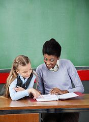 Image showing Schoolgirl Pointing In Binder With Teacher At Desk