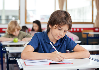 Image showing Schoolboy Writing In Book At Desk