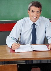 Image showing Male Teacher Sitting With Pen And Binder At Desk