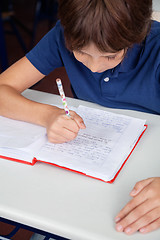 Image showing Little Schoolboy Reading Book At Desk