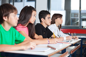 Image showing Teenage Students Looking Away While Studying At Desk