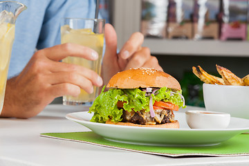 Image showing Burger With Man's Hand Holding Drink At Table