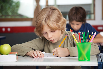 Image showing Schoolboy Writing In Book At Desk