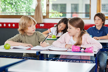 Image showing Schoolboy Looking At Girl While Writing At Desk