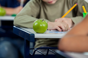 Image showing Schoolboy Writing In Book With Apple At Desk