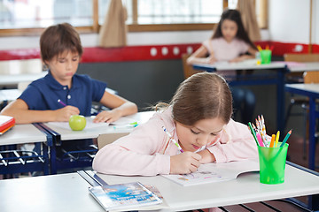 Image showing Schoolgirl Drawing While Leaning On Desk In Classroom