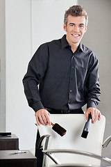 Image showing Happy Hairdresser Holding Straightener And Brush