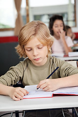 Image showing Cute Schoolboy Writing In Book At Desk
