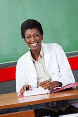 Image showing Happy Teacher With Pen And Binder Sitting At Desk