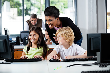 Image showing Happy Teacher Assisting Schoolchildren In Using Computer