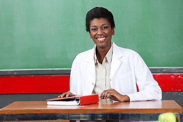 Image showing Happy Teacher Sitting With Binder At Desk In Classroom