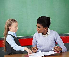 Image showing Schoolgirl And Teacher Looking At Each Other At Desk