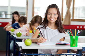 Image showing Schoolgirl Writing In Book At Classroom