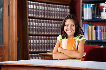 Image showing Schoolgirl Holding Book While Sitting At Table In Library