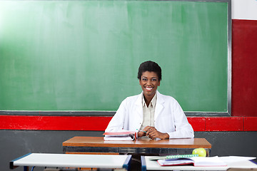 Image showing Happy Teacher Sitting At Desk In Classroom