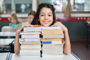 Image showing Happy Schoolgirl Resting Chin On Stacked Books At Desk