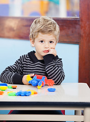 Image showing Bored Boy Holding Blocks Sitting At Desk In Classroom