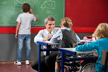 Image showing Teacher Looking At Schoolgirl While Crouching At Desk