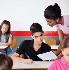 Image showing Teacher Showing Paper To Male Student At Desk