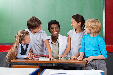 Image showing Teacher Sitting At Desk With Students At Desk