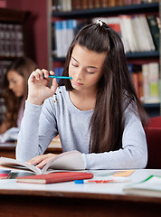 Image showing Schoolgirl Holding Pen While Reading Book In Library