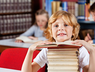 Image showing Schoolboy With Stack Of Books Sitting In Library