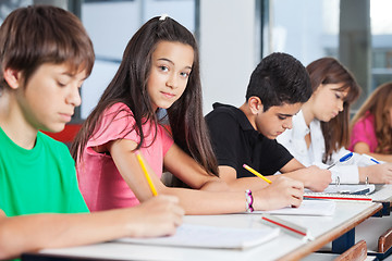 Image showing Teenage Girl Sitting With Classmates Writing At Desk