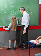 Image showing Little Girl Writing On Board With Teacher Assisting Her