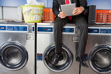 Image showing Businessman Using Digital Tablet While Sitting On Washing Machin