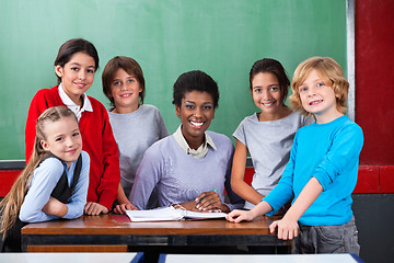 Image showing Teacher And Schoolchildren Smiling Together At Desk In Classroom