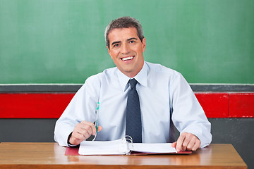 Image showing Happy Male Teacher With Pen And Binder Sitting At Desk