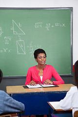 Image showing Teacher Sitting At Desk With Students In Foreground