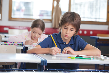 Image showing Little Boy Writing Notes With Classmate In Background