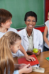 Image showing Teacher Holding Apple With Students Standing At Desk
