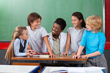 Image showing Happy Teacher With Students Communicating At Desk
