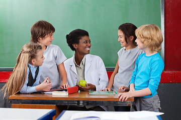 Image showing Schoolchildren Looking Teacher Sitting At Desk