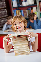 Image showing Schoolboy Smiling While Sitting With Stack Of Books In Library