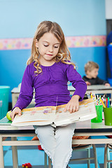 Image showing Girl Reading Book While Sitting On Desk At Kindergarten