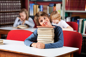 Image showing Cute Schoolboy Sitting With On Stack Of Books At Table In Librar