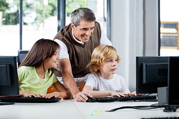 Image showing Happy Teacher Assisting Schoolchildren In Using Desktop Pc