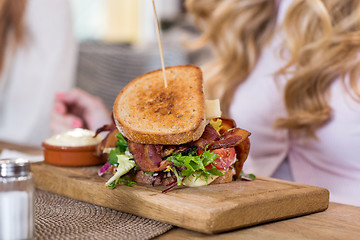 Image showing Sandwich On Wooden Plate With Women In Background