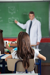 Image showing Girl Sitting At Desk With Teacher Teaching In Background