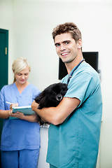 Image showing Veterinarian Doctor Carrying A Dog With Female Nurse Writing On